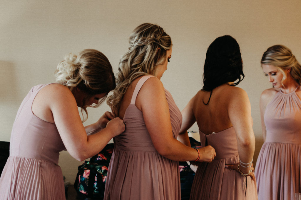 bridesmaids helping each other do up their dresses