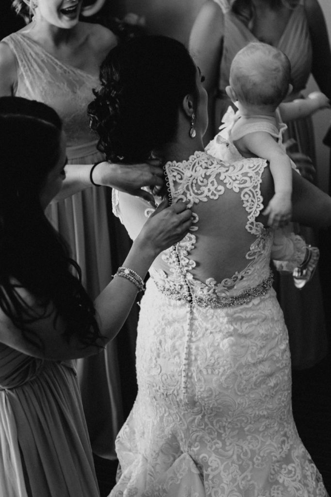 sister of the bride doing up brides dress, black and white image