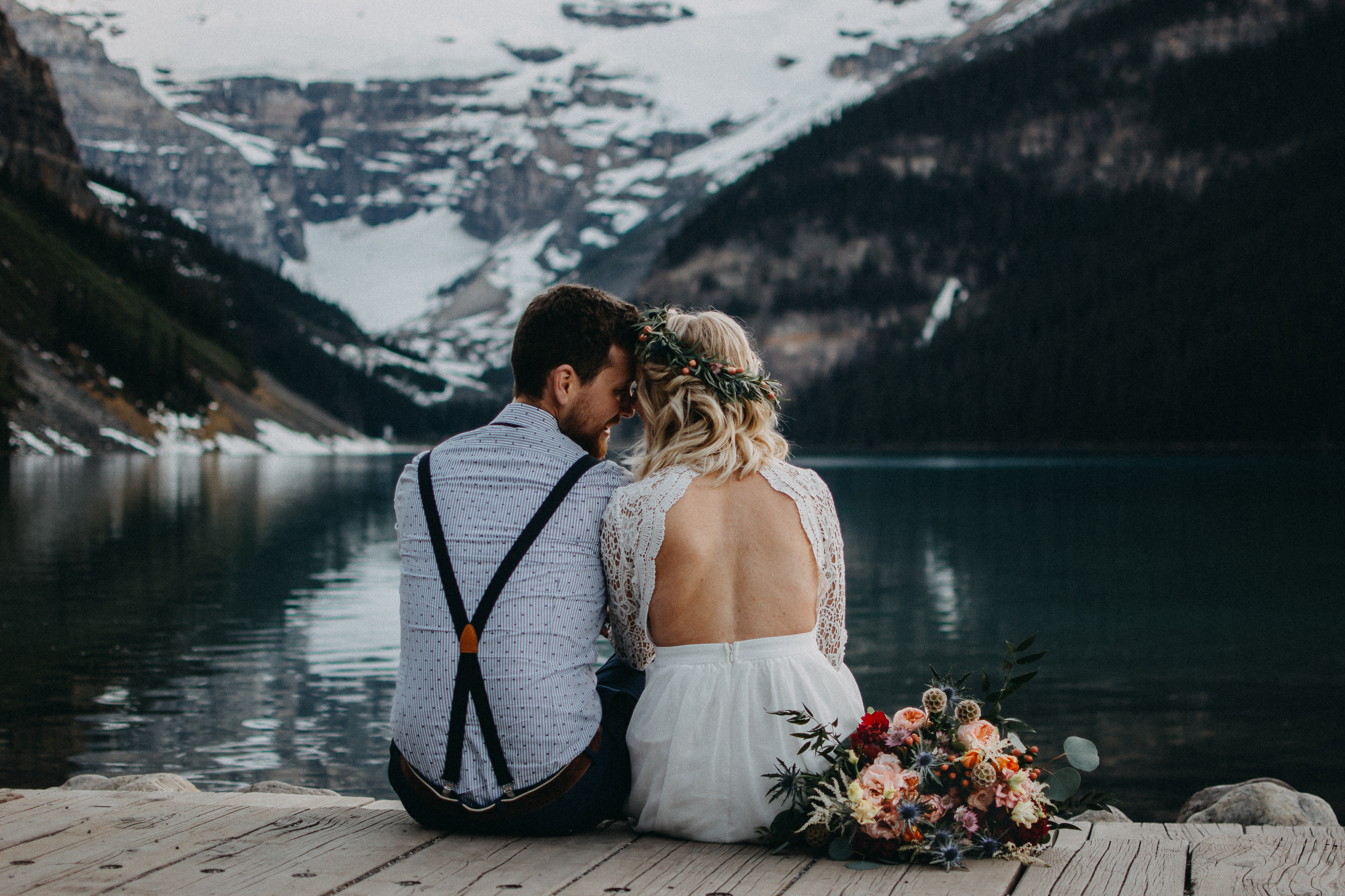 The bride and groom sitting on the dock at Lake Louise, Alberta, with their backs to the camera