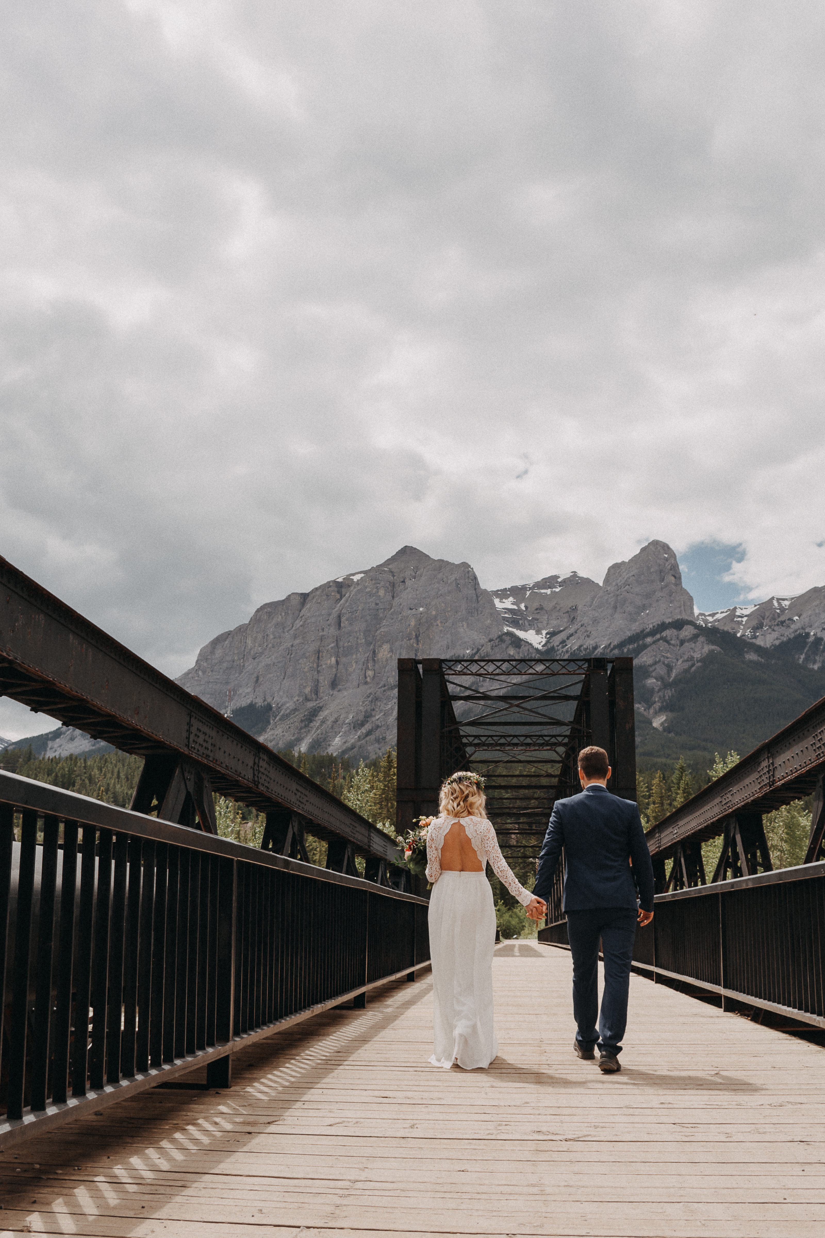 The bride and groom walking away from the camera, hand in hand, on the engine bridge in Canmore, Alberta