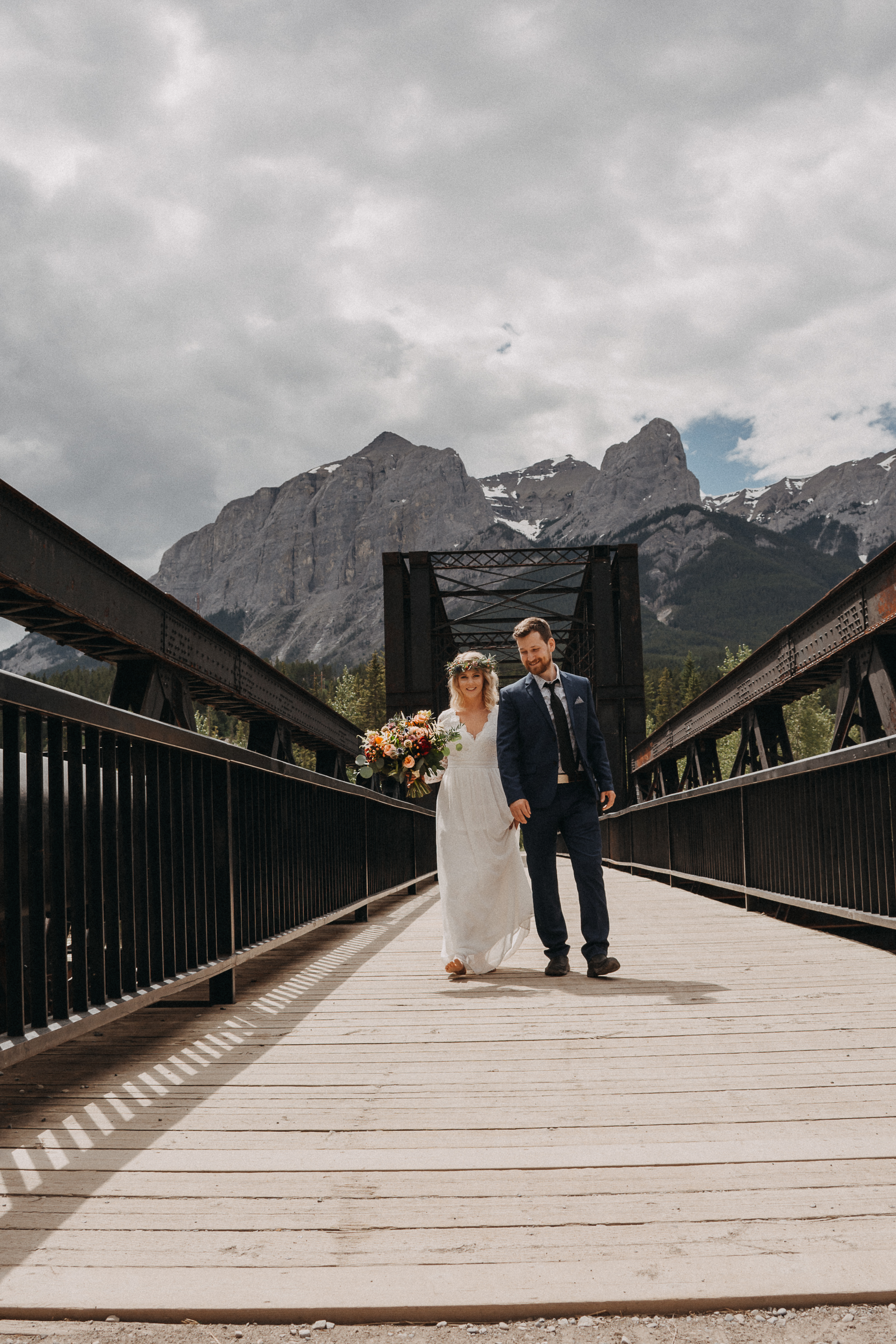 The bride and groom walking towards the camera, hand in hand, on the engine bridge in Canmore, Alberta