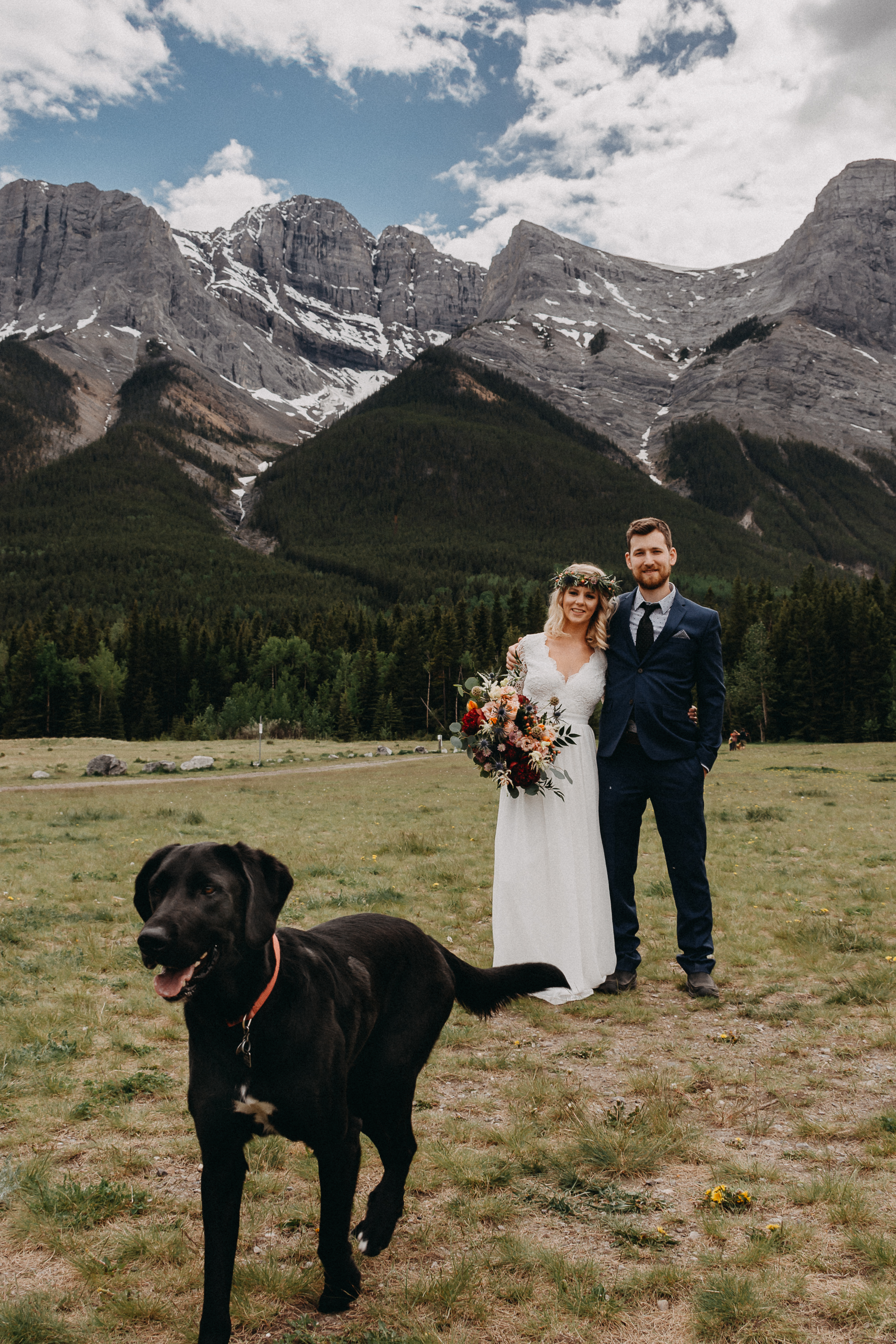 The bride and groom holding each other and their dog in front of the rocky mountains