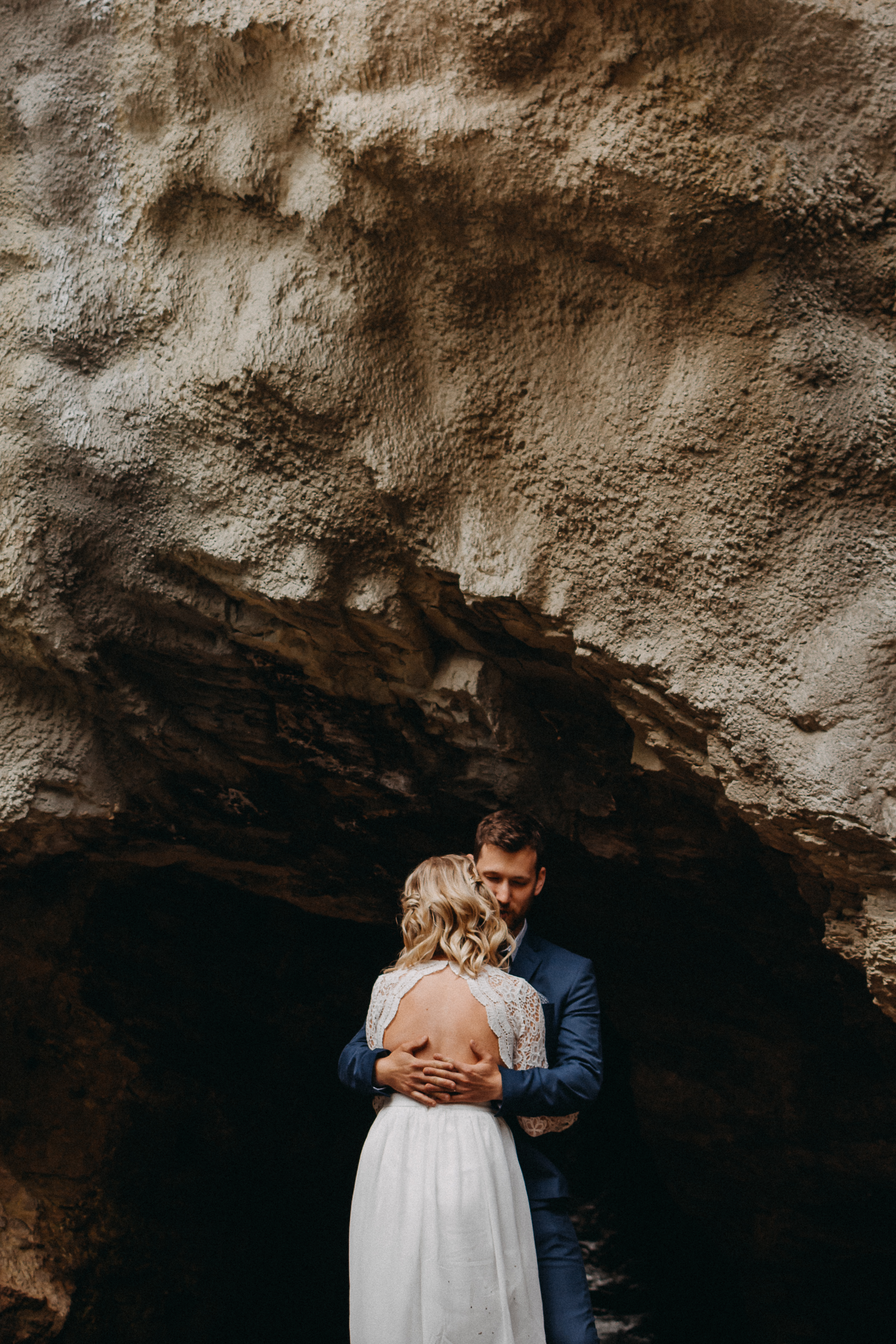 The bride and groom holding each other in front of a cave