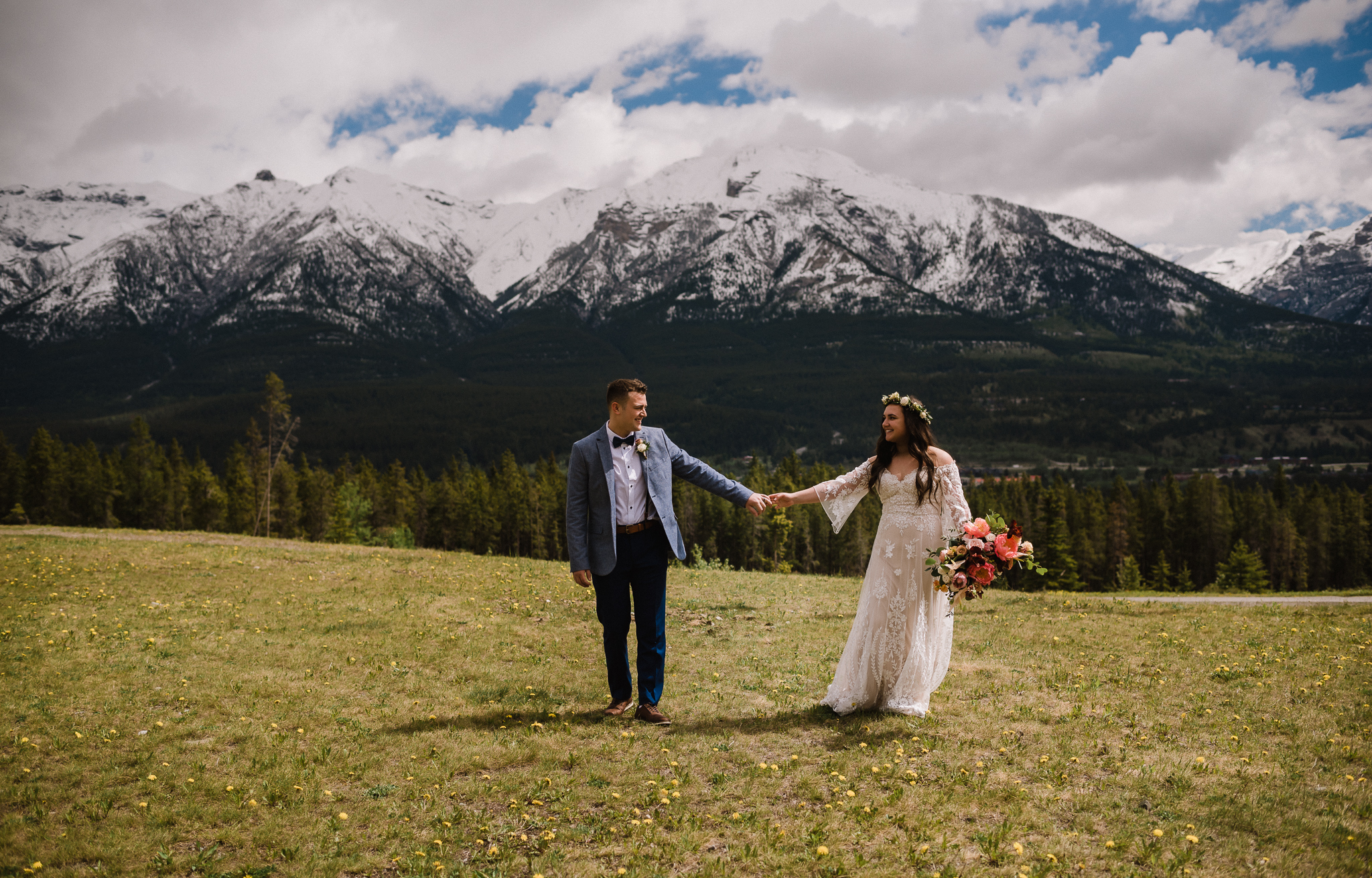 Bride and groom holding hands in front of mountain backdrop at the Nordic Center, Canmore