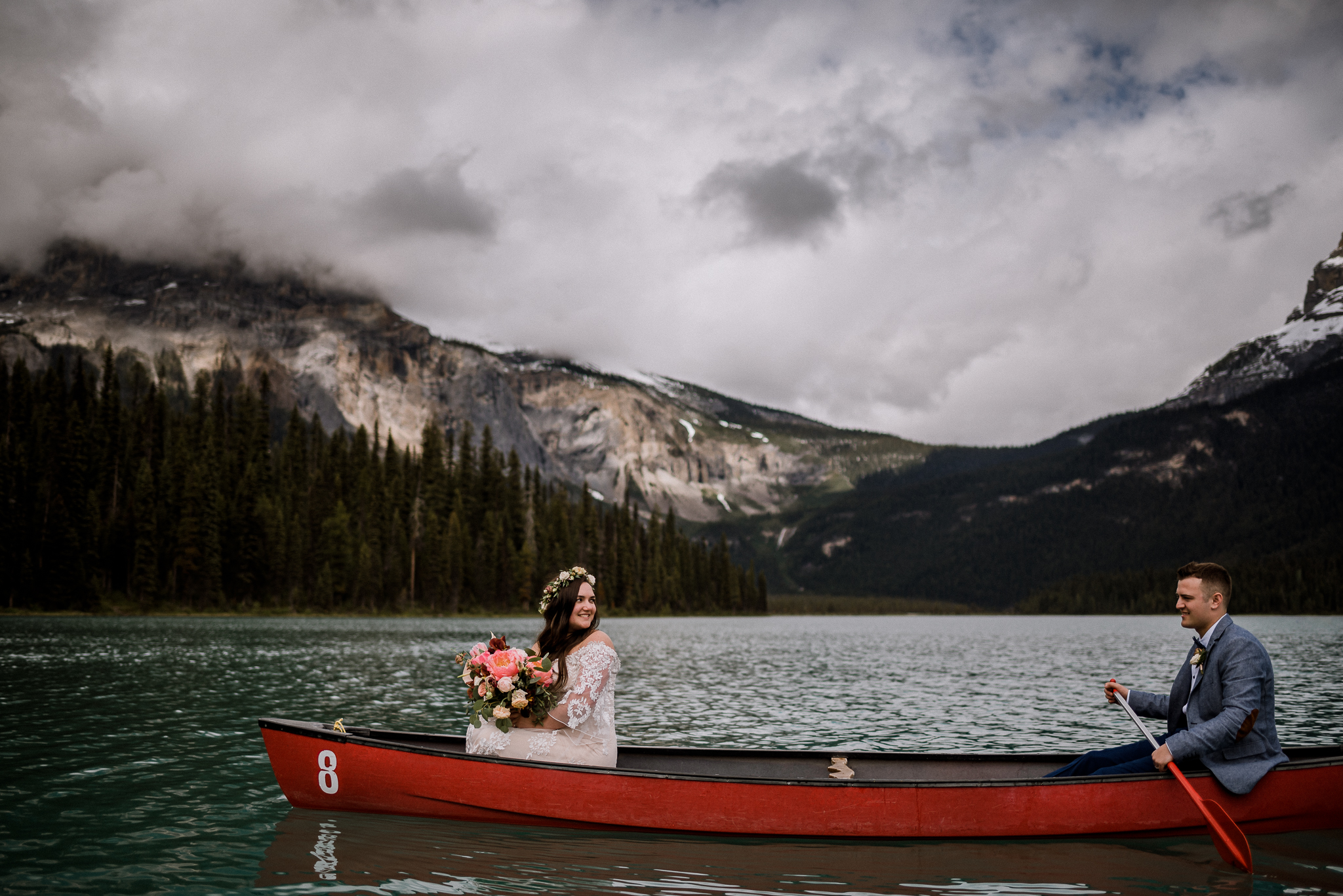 Bride looking back at her groom in a red canoe holding bouquet at Emerald Lake, BC