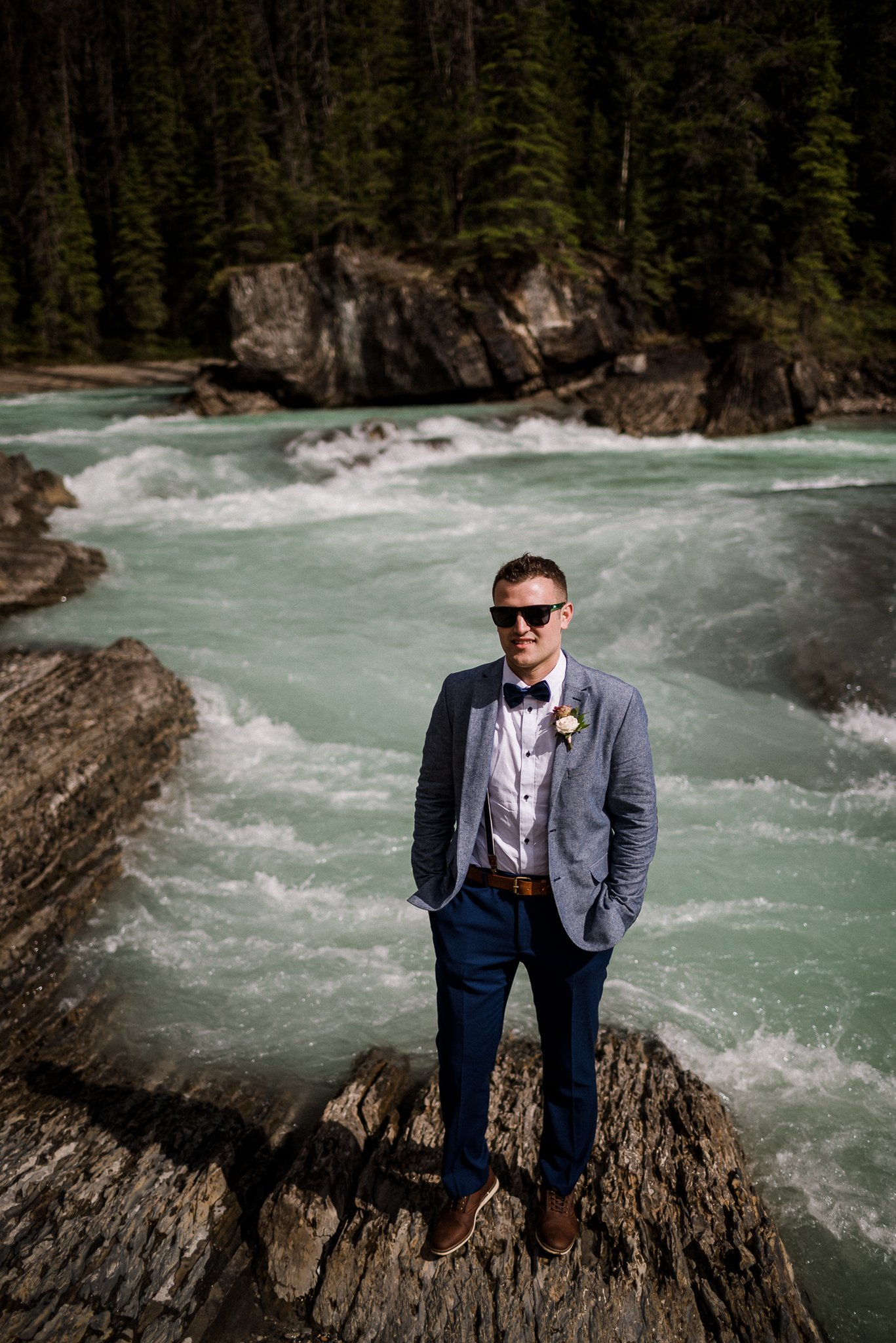Groom wearing sunglasses in front of river at Yoho National Park