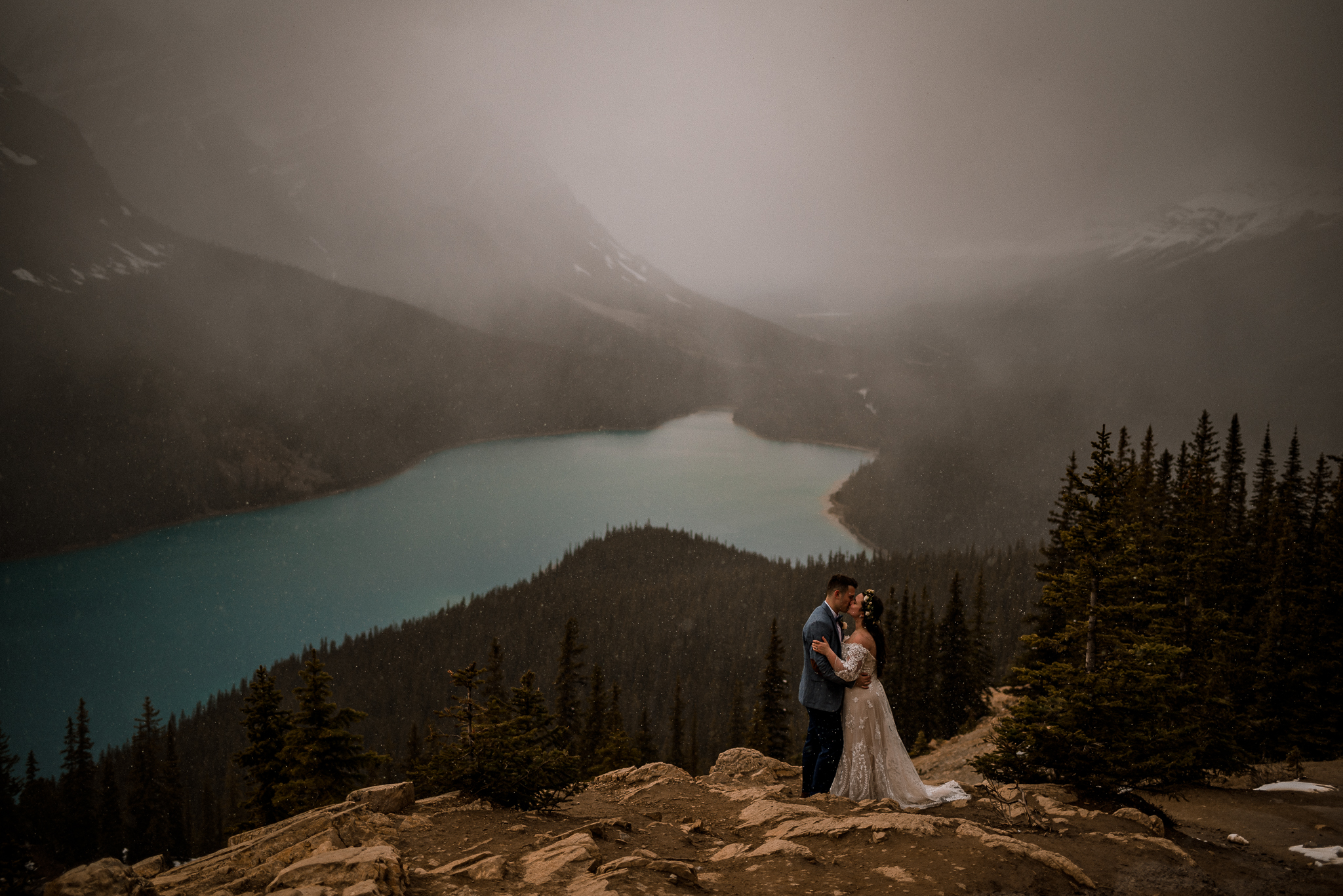 Snow falls while bride and groom kiss at Peyto Lake, Alberta