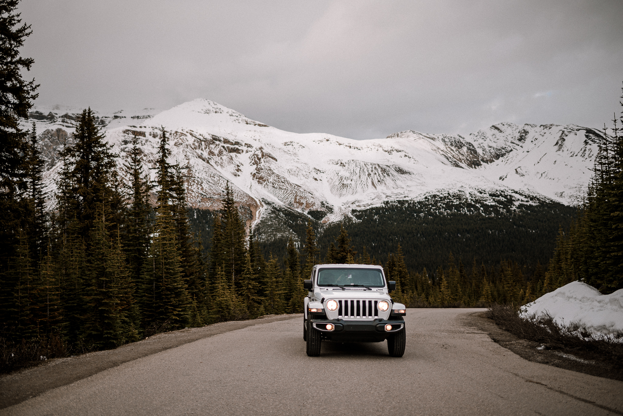 White Jeep with lights turned on in front of mountain range