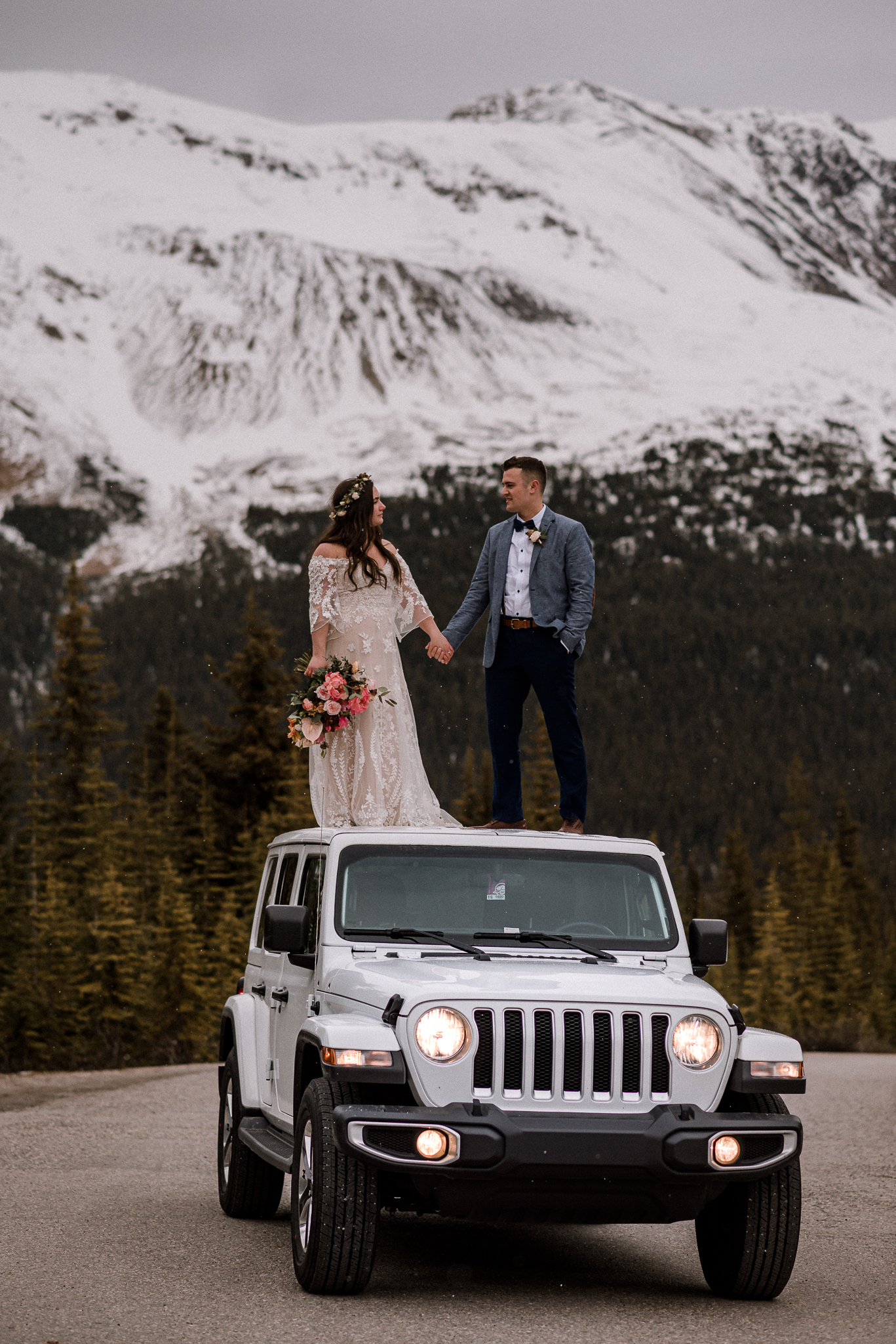 Bride and groom standing on top of white keep in front of a mountain range