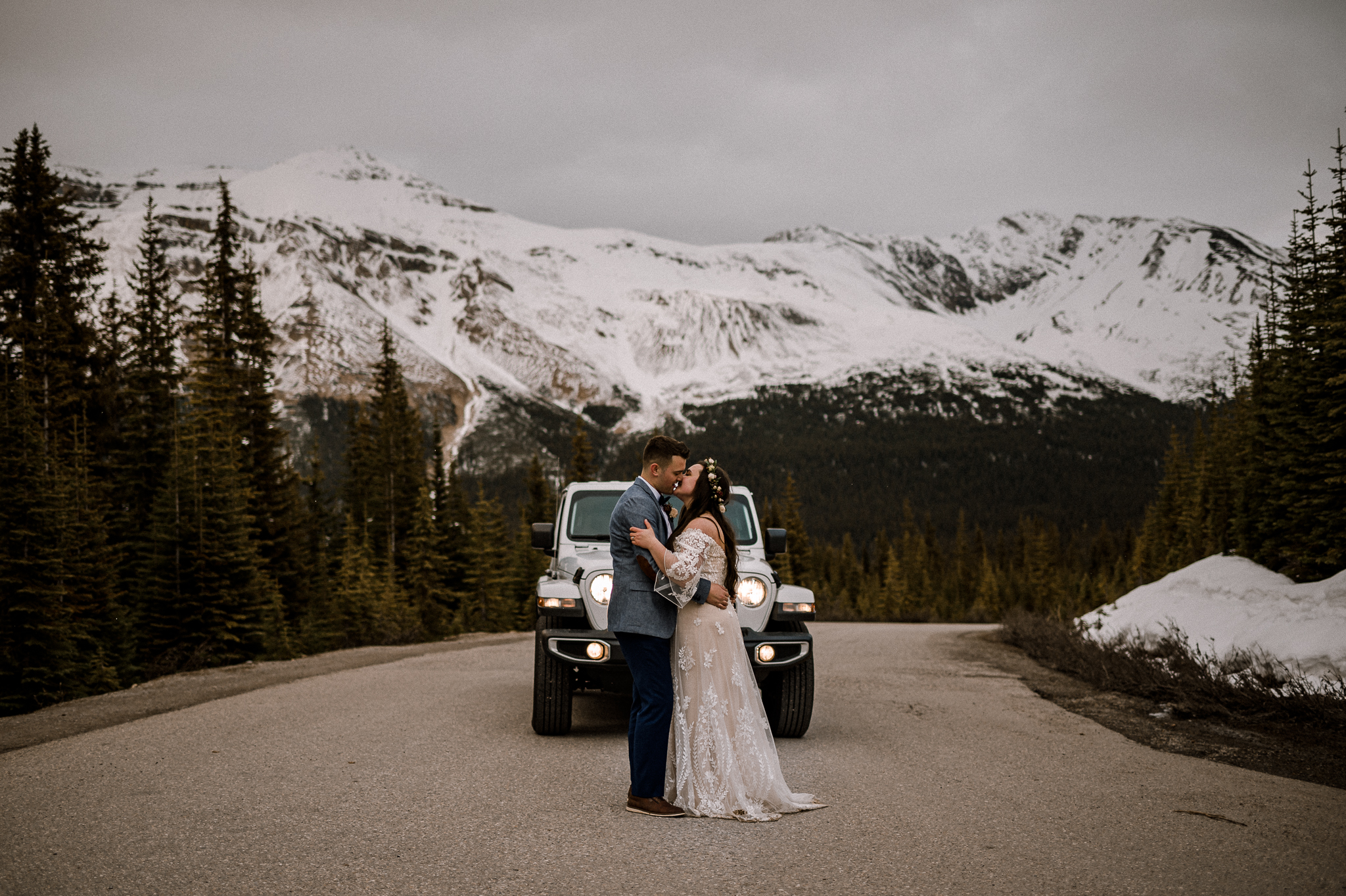 Bride and groom kissing in front of white Jeep and mountain background