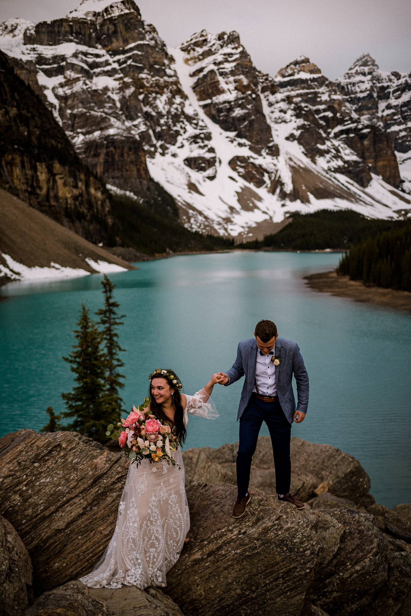 Groom helping bride up on to rock at Moraine Lake, Alberta