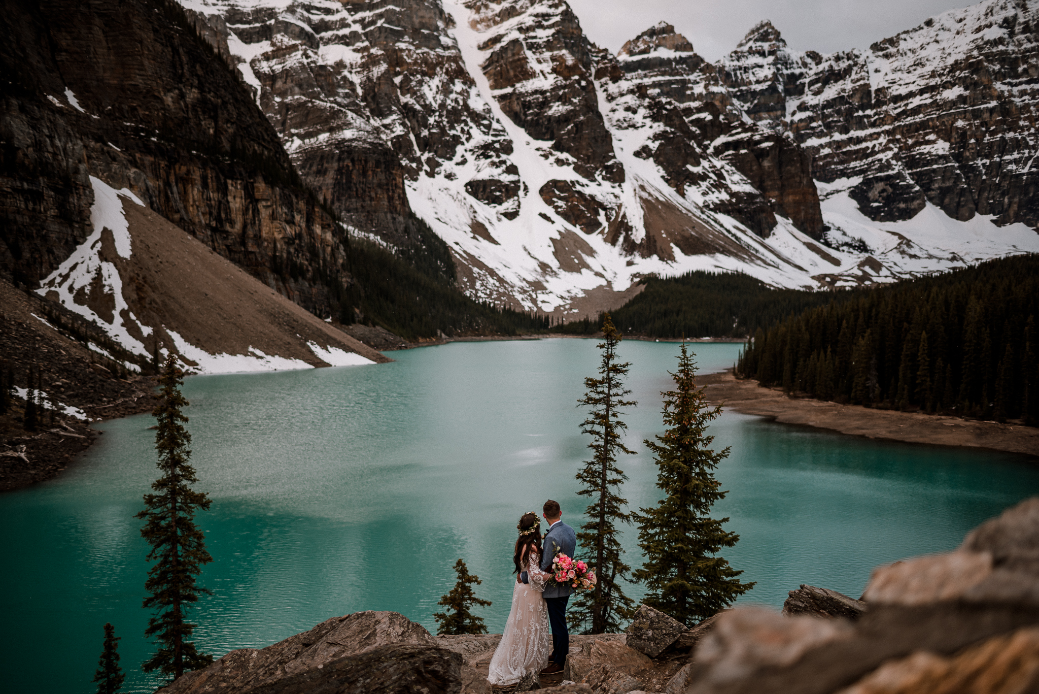 Bride and groom standing on a rock looking at the mountains at Moraine Lake, Alberta