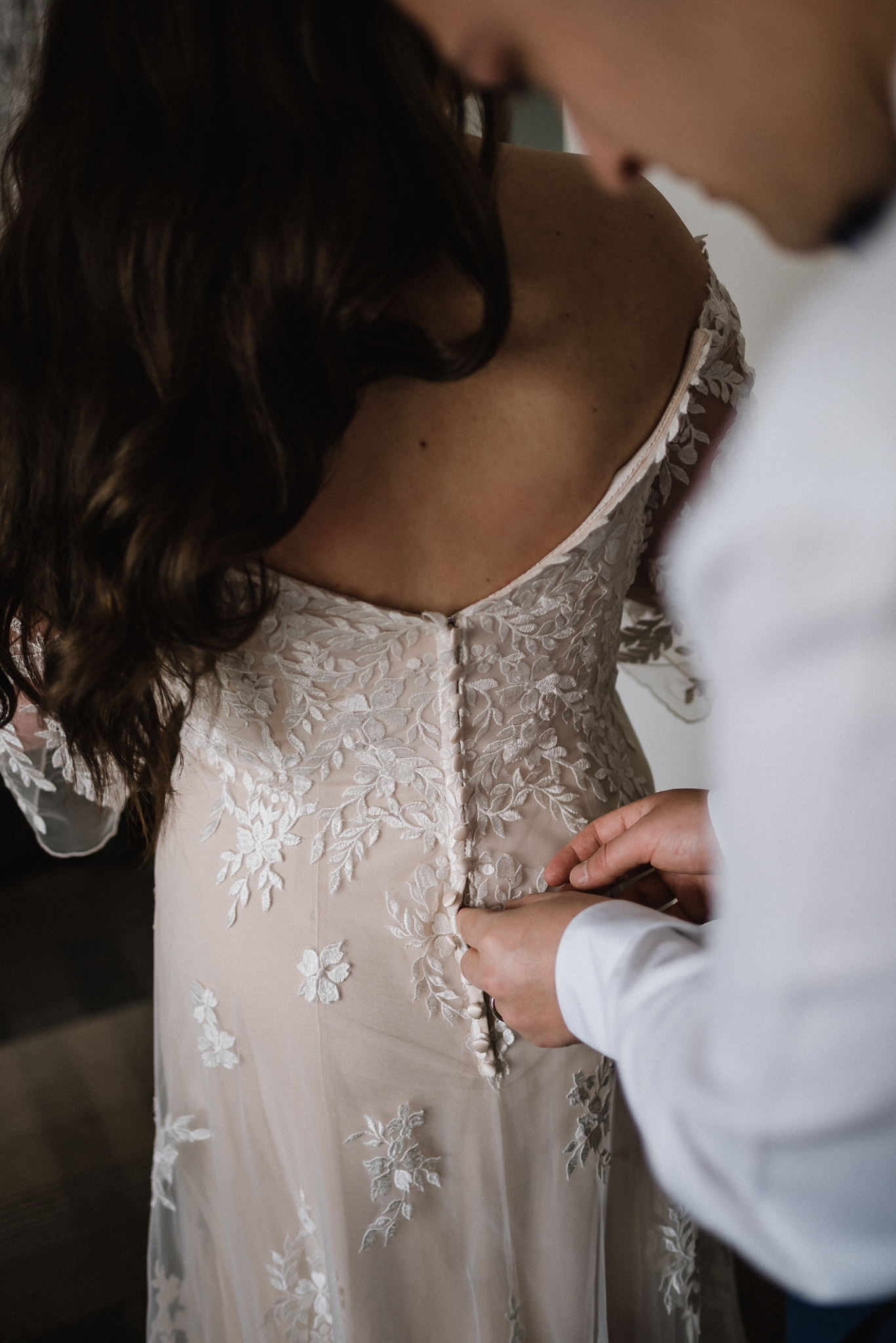 Groom helping bride with buttons on her dress at Coast Canmore Hotel, Alberta