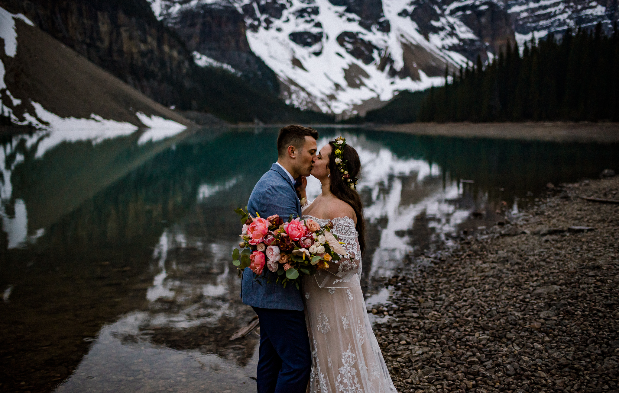 Groom kissing bride while she holds bouquet in front of Moraine Lake