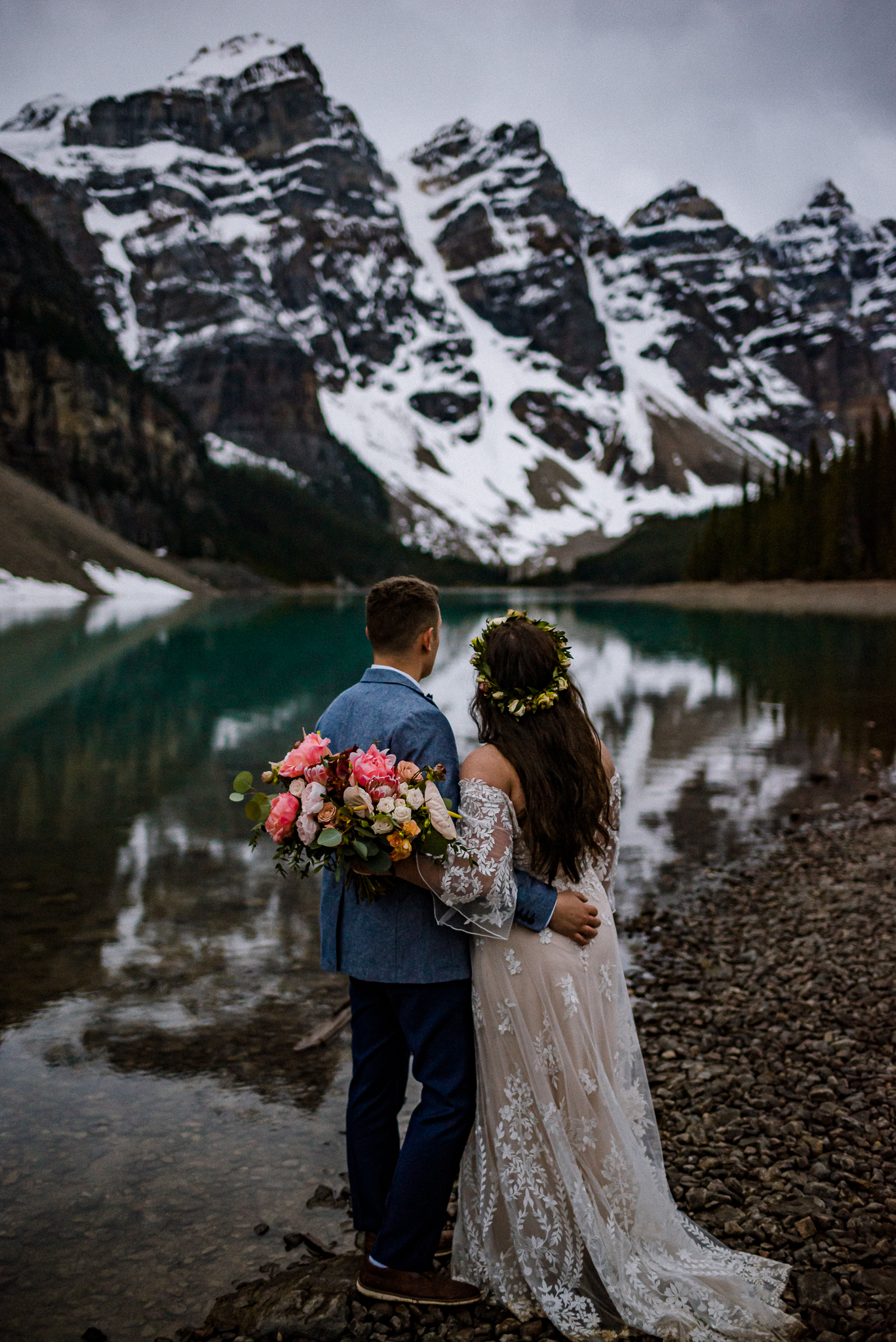 Groom holding his bride while she holds bouquet at Moraine Lake, Alberta